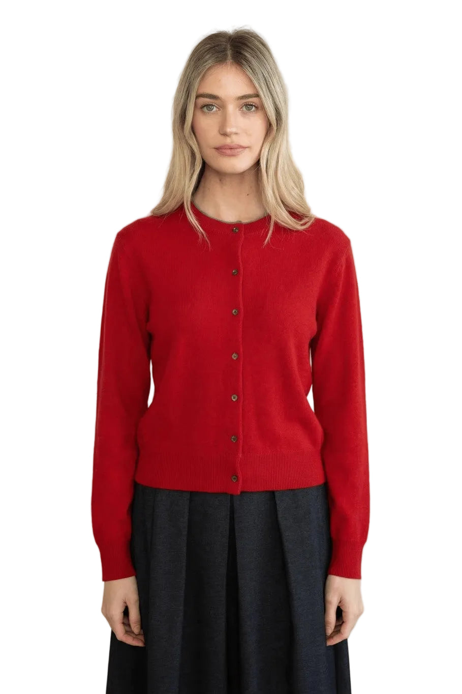 A woman modeling a bright red button-up cardigan sweater with dark buttons, paired with a dark pleated skirt, against a neutral light beige background.