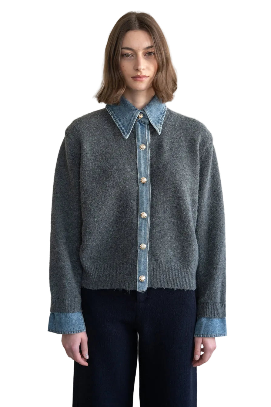 A model wearing a gray knit button-up cardigan with light blue denim collar, cuffs, and front placket, paired with dark pants, set against a plain light beige wall.
